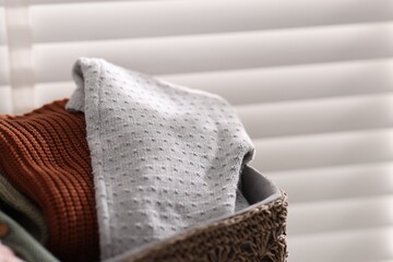 Wool baby clothes in basket on light background, closeup