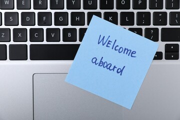Paper note with words Welcome Aboard on laptop, top view