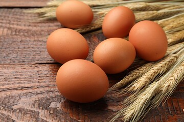 Raw eggs and spikes of wheat on wooden table, closeup