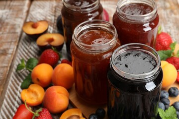 Different jams in jars and ingredients on wooden table, closeup
