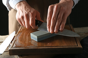 Man sharpening knife with sharpener on wooden table, closeup