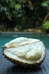 Fresh ripe durian on wicker table near swimming pool outdoors, closeup