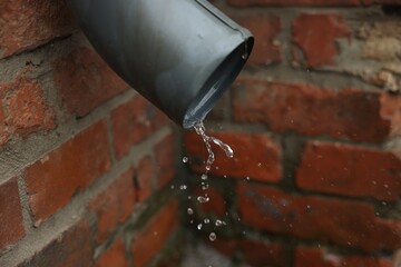 Water dripping from drain pipe outdoors, closeup