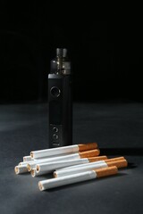Electronic smoking device and cigarettes on dark table against black background, closeup