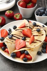Tasty crepes with strawberries, blueberries and chocolate sauce on gray textured table, closeup
