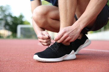Man tying shoelace of black sneaker at stadium, closeup. Space for text