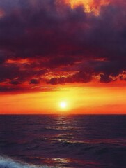 Obraz premium Vibrant sunset over the calm ocean with dramatic dark clouds and glowing orange sky reflecting on water