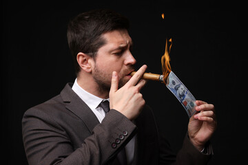 Greedy businessman lighting cigar with dollar banknote on black background