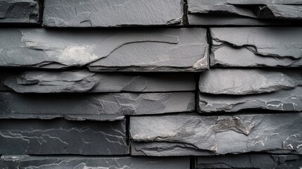 Close-up of dark gray stacked slate stones arranged tightly with natural rough textures and layered edges creating a solid stone wall