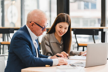 Two business colleagues working together on documents at table with laptop, showing collaboration and focus in modern office environment