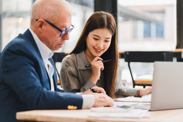 Two business colleagues working together on documents at table with laptop, showing collaboration and focus in modern office environment