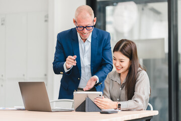 Two business colleagues smiling and discussing work using tablet and laptop in modern office, showing collaboration and positive teamwork atmosphere