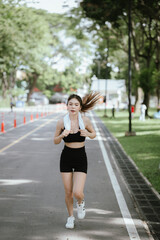 Obraz premium A young woman is jogging outdoors in a park, wearing workout clothes. She is surrounded by nature and sunlight. She enjoys exercise, fresh air, energy and healthy living.