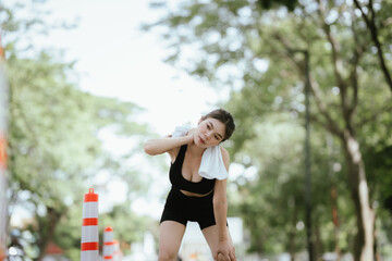 A fit woman cools down after an intense outdoor workout, wiping sweat with a towel. She embodies...