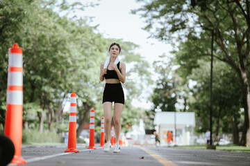 Obraz premium A young woman is jogging outdoors in a park, wearing workout clothes. She is surrounded by nature and sunlight. She enjoys exercise, fresh air, energy and healthy living.