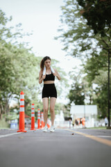 Obraz premium A young woman is jogging outdoors in a park, wearing workout clothes. She is surrounded by nature and sunlight. She enjoys exercise, fresh air, energy and healthy living.