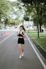 Obraz premium A young woman is jogging outdoors in a park, wearing workout clothes. She is surrounded by nature and sunlight. She enjoys exercise, fresh air, energy and healthy living.