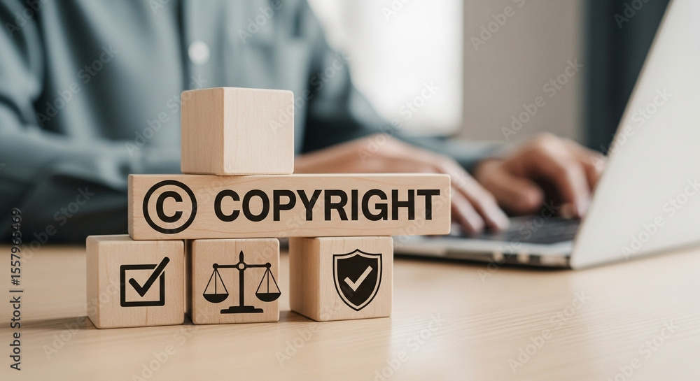 Poster copyright concept with wooden blocks stacked on a desk near a person using a laptop computer
