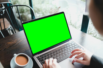 Over the shoulder view of a person using a laptop with a blank green screen in a cafe. A chroma key...