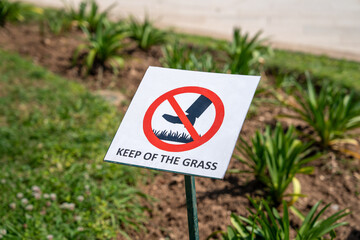 A sign with a red prohibition symbol warns to keep off the grass in a garden setting. the image emphasizes the importance of protecting landscaped areas.