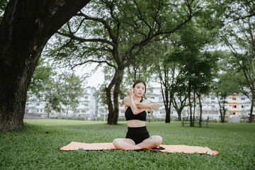 A young woman practices yoga outdoors in a peaceful urban park, promoting wellness, balance, and mindfulness through stretching exercises on a mat surrounded by nature and tranquility.