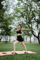 A young woman practices yoga outdoors in a peaceful urban park, promoting wellness, balance, and mindfulness through stretching exercises on a mat surrounded by nature and tranquility.