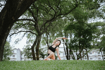 A young woman practices yoga outdoors in a peaceful urban park, promoting wellness, balance, and mindfulness through stretching exercises on a mat surrounded by nature and tranquility.
