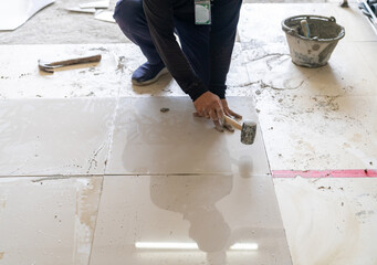 The worker uses a rubber mallet to tap the tiles into level