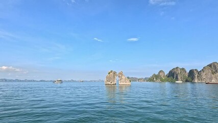 Panning shot of majestic limestone islets, the Kissing Rocks in Ha Long Bay, Vietnam in clear blue sky.	
