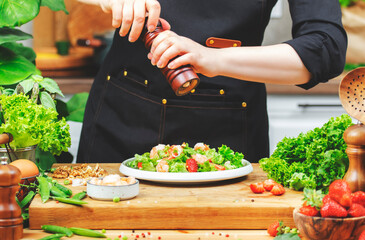 Chef woman prepares colorful salad in modern kitchen, showcasing fresh vegetables and aromatic herbs while seasoning with care.