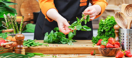 Female chef prepares fresh basil, herbs and vegetables in a bright kitchen for a healthy vegan dish, emphasizing natural ingredients and cooking techniques