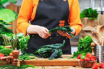 woman prepares fresh tuscan kale in a bright kitchen, showcasing her passion for healthy vegan cooking with vibrant ingredients.