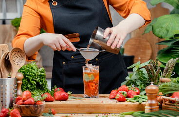 Chef prepares a refreshing herbal nojito drink with fresh strawberries and basil in a vibrant kitchen setting