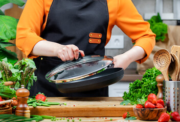 talented woman chef skillfully lifts a pot lid while preparing a nutritious vegan dish surrounded by vibrant vegetables in her kitchen.