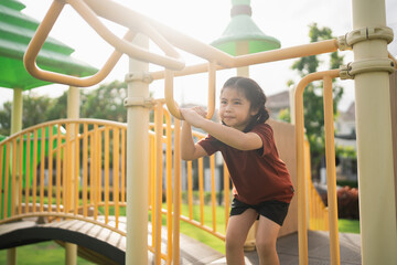 Obraz premium Young girl climbing playground equipment under bright sunlight enjoying outdoor activity in a vibrant park setting with green trees and playful environment