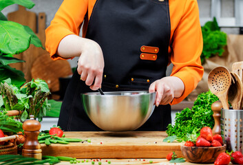 woman chef skillfully mixes ingredients in a metal bowl for a healthy meal in a lively kitchen