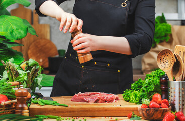 chef sprinkle beef steak with pepper from the mill prepares a healthy dish in a cozy kitchen, using fresh farm herbs and vegetables