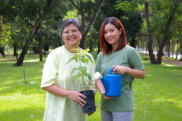 Volunteer elderly mother and daughter holding saplings to help restore forests. World Environment Day. Save the world. Plant trees to reduce global warming. Green ecosystem.
