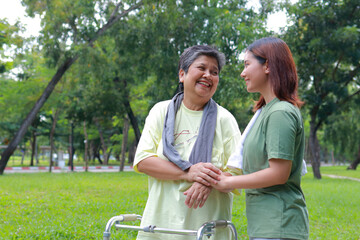 An elderly Asian woman walks with a cane in an outdoor park, with her daughter or a physical therapist taking care of her. Health care center for the elderly. copy space