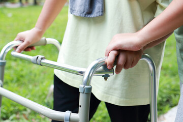 Close-up view of elderly woman using cane to walk, exercising in outdoor garden with hands of daughter or physical therapist.  Health care center for the elderly.