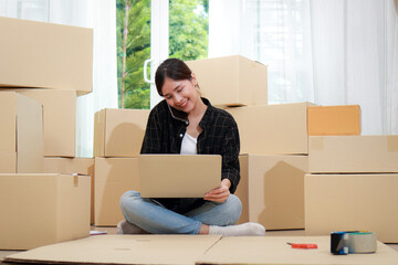Beautiful Asian female entrepreneur doing online business, talking on the phone and checking product information on laptop computer. Online business concept. Sme business.