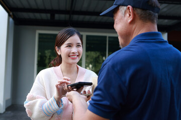 Asian woman signing on digital smartphone after receiving package from delivery man in blue shirt holding package box at doorstep. Freight forwarding, parcel.