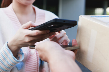 Asian woman scans barcode on digital smartphone to pay after receiving package from delivery man at doorstep. Freight, Parcel.