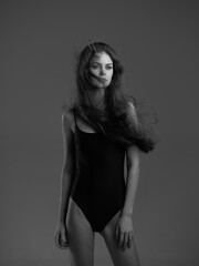 black and white woman wearing black bodysuit stands with flowing hair against gray background in...