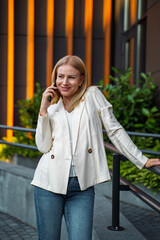 Beautiful blonde business woman in front of office building talking on the phone 