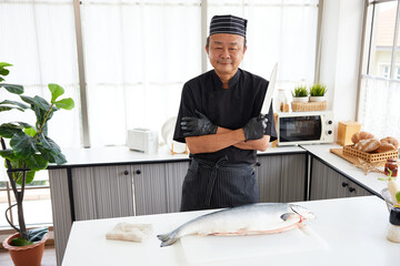 chef holding knife with a big raw salmon in the kitchen