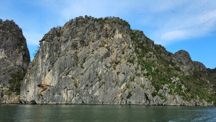 Stunning limestone island rising from emerald water in Ha Long Bay, Vietnam, beneath a sky streaked...