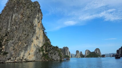 Fototapeta premium Stunning limestone island rising from emerald water in Ha Long Bay, Vietnam, beneath a sky streaked with soft clouds.