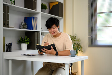 Asian man writing thoughts in a personal diary while enjoying a calm morning at home