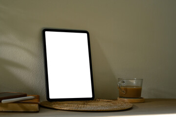 Digital tablet with blank screen on wooden table next to books with soft shadows